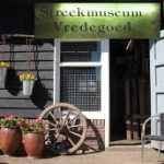 ingang van Streekmuseum Vredegoed met twee bloempotten en een oud wiel naast de deur